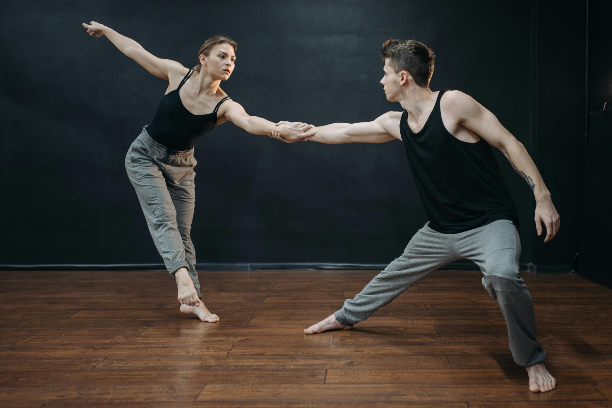Two dancers reaching toward each other in a dark studio